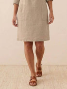 Beige cotton dress with pockets, knee-length and 3/4 sleeves rolled below elbow, styled with brown sandals, perfect for summer comfort and understated elegance.