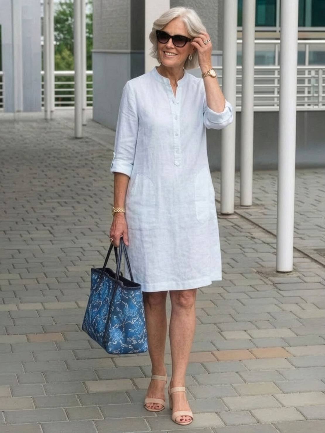 Woman wearing white knee-length cotton dress with rolled ¾ sleeves and carrying blue handbag outdoors